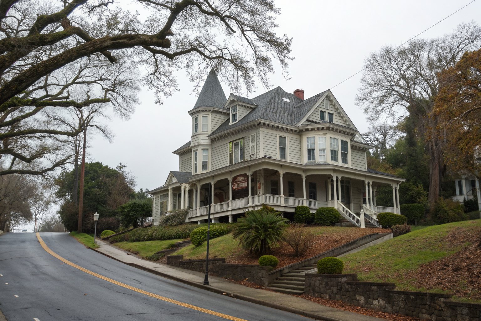A large Victorian house with a turret and wide porch on a tree-lined hillside street