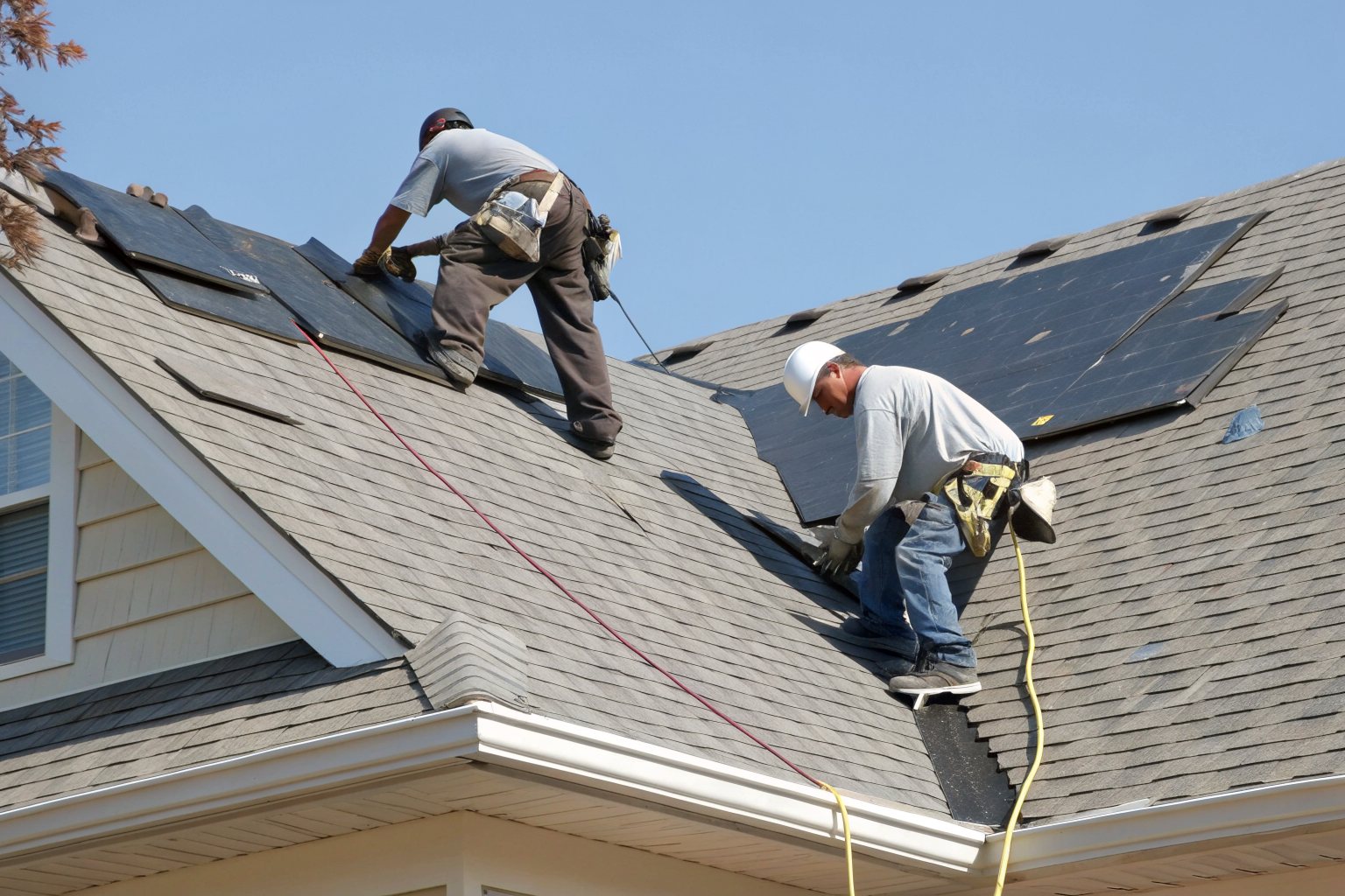 Two roofers laying new charcoal architectural shingles on a two-story house